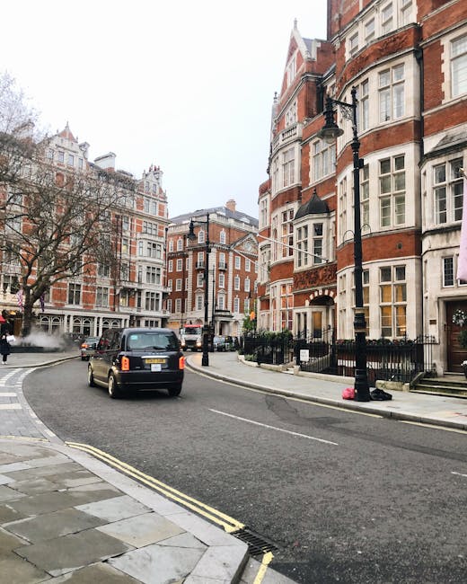 Street scene in Knightsbridge, Brompton Road with classic red-brick Victorian-style residential buildings featuring white window frames and decorative stonework. The pavement is made of grey stone slabs, and the street surface is asphalt with visible double yellow lines along the curb. A black taxi is driving on the road, and lampposts line the sidewalk. The overall scene depicts a quiet, clean, urban residential area with well-maintained architecture, captured during a cloudy day. Knightsbridge Carpet Cleaners specializes in surface cleaning and deep cleaning solutions, ensuring hygiene and cleanliness for both homes and commercial spaces in this prestigious district.